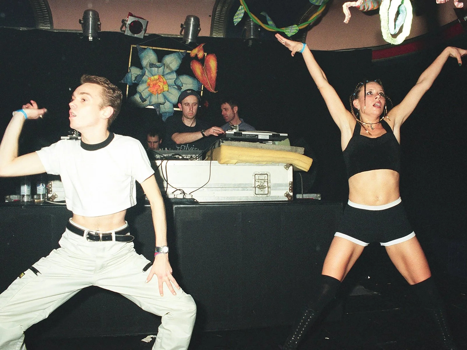 Dancers performing on stage at underground rave event with DJ in background