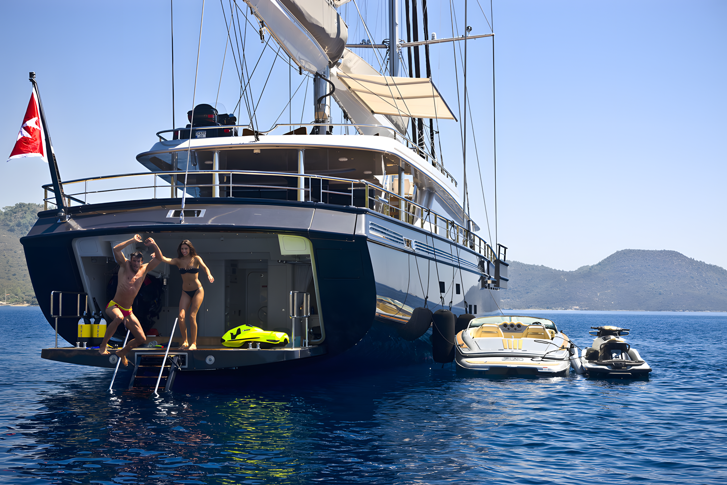 People jumping off the back of a luxury yacht into the water on a sunny day with mountainous landscape in the background.