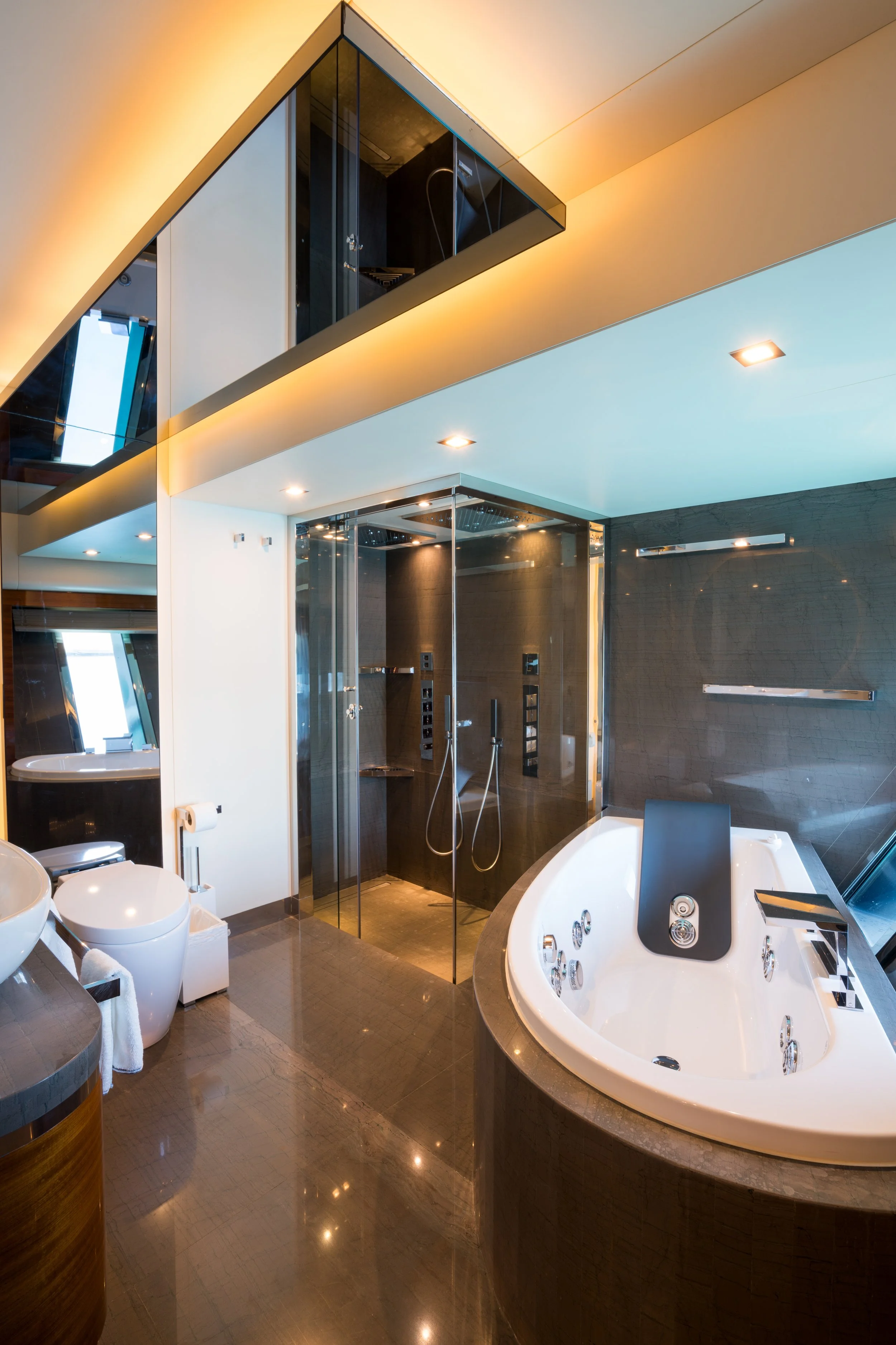 Modern bathroom with a shower, bathtub, and toilet, featuring dark wood and glass accents, illuminated by ceiling lights.