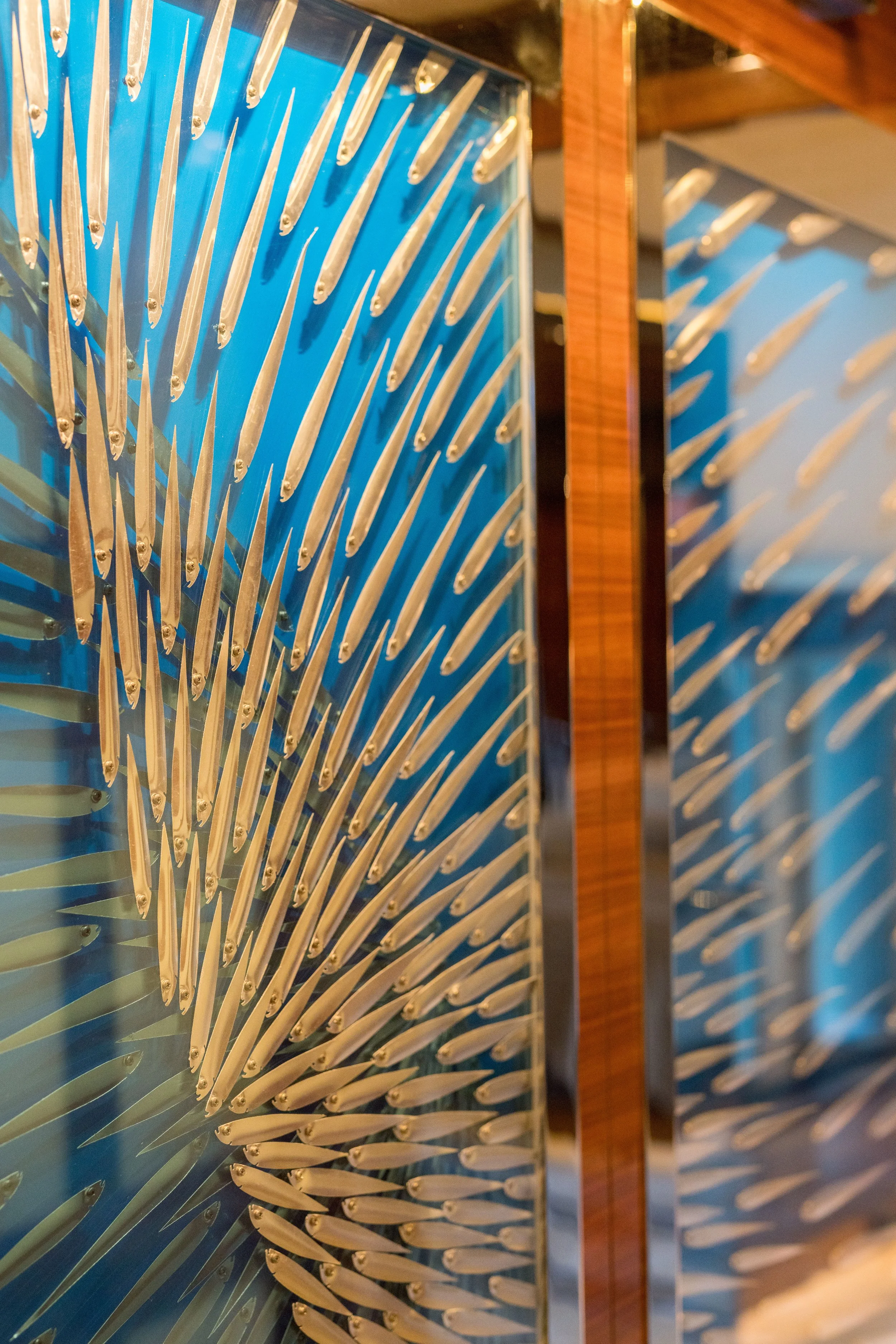 Close-up of colorful abstract art with metallic elements on a blue background, framed by wooden borders.