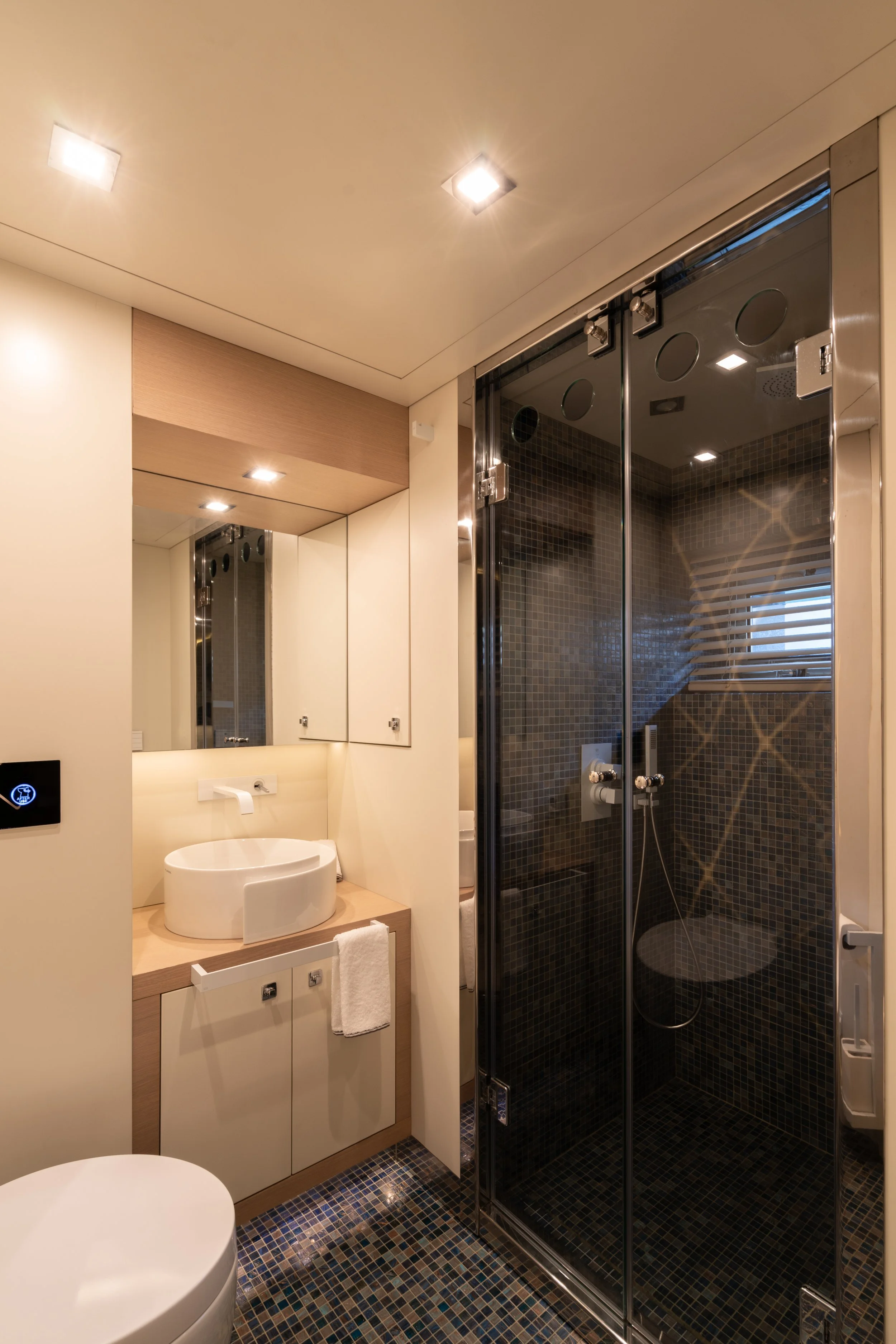 Modern bathroom with a glass-enclosed shower, white sink, mirror, and beige cabinets.