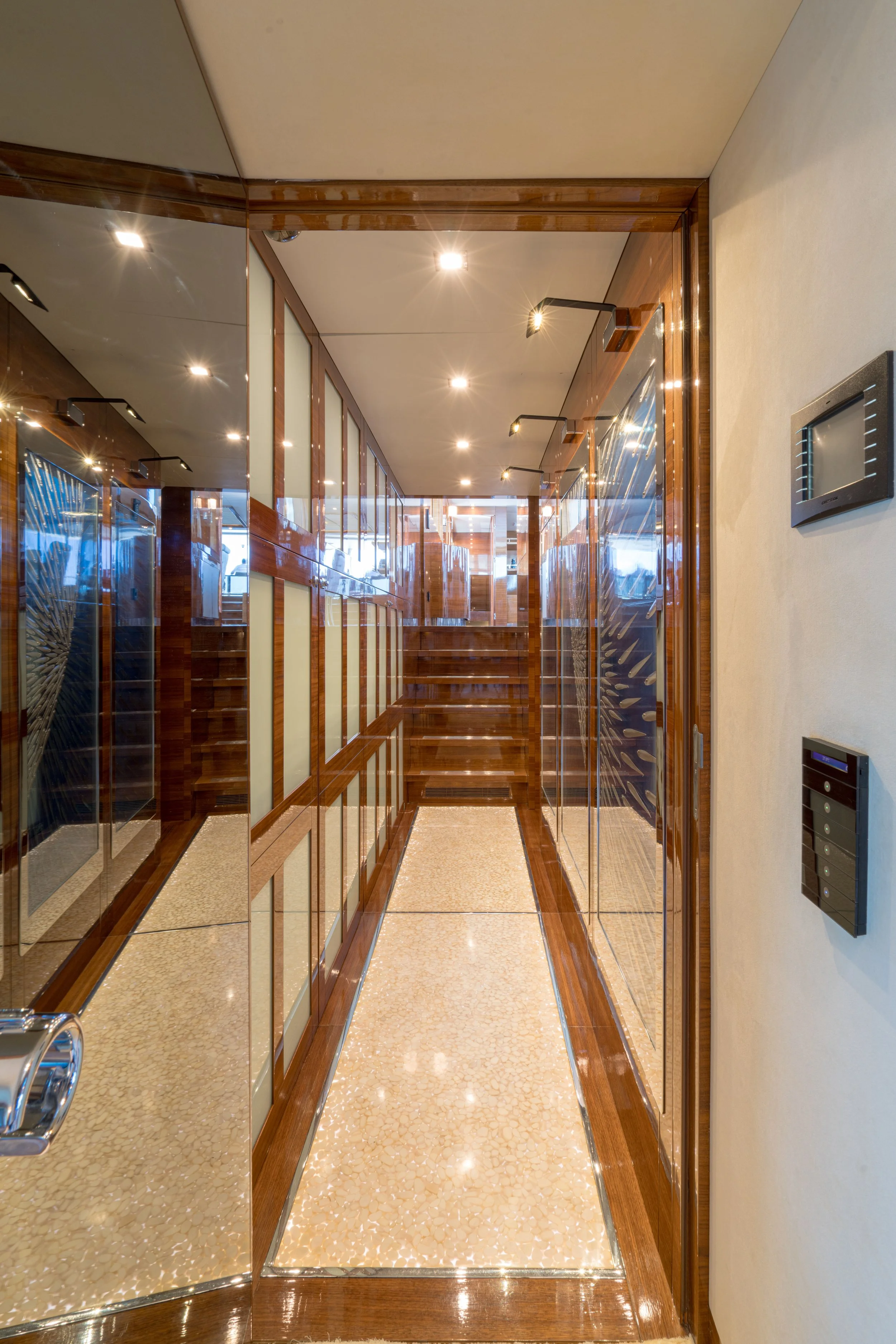 A narrow hallway with wooden and mirrored walls, polished tile flooring, and ceiling spotlights.