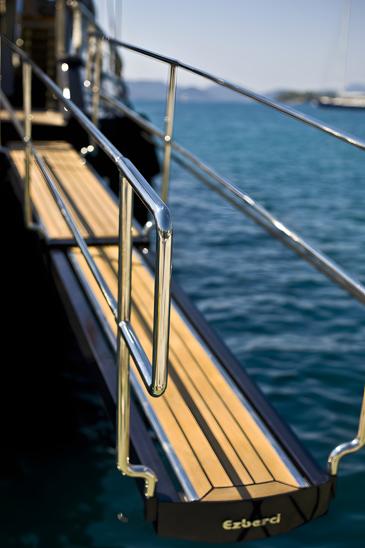 A wooden and metal gangway on a boat leading to the water with a distant shoreline and mountain in the background.