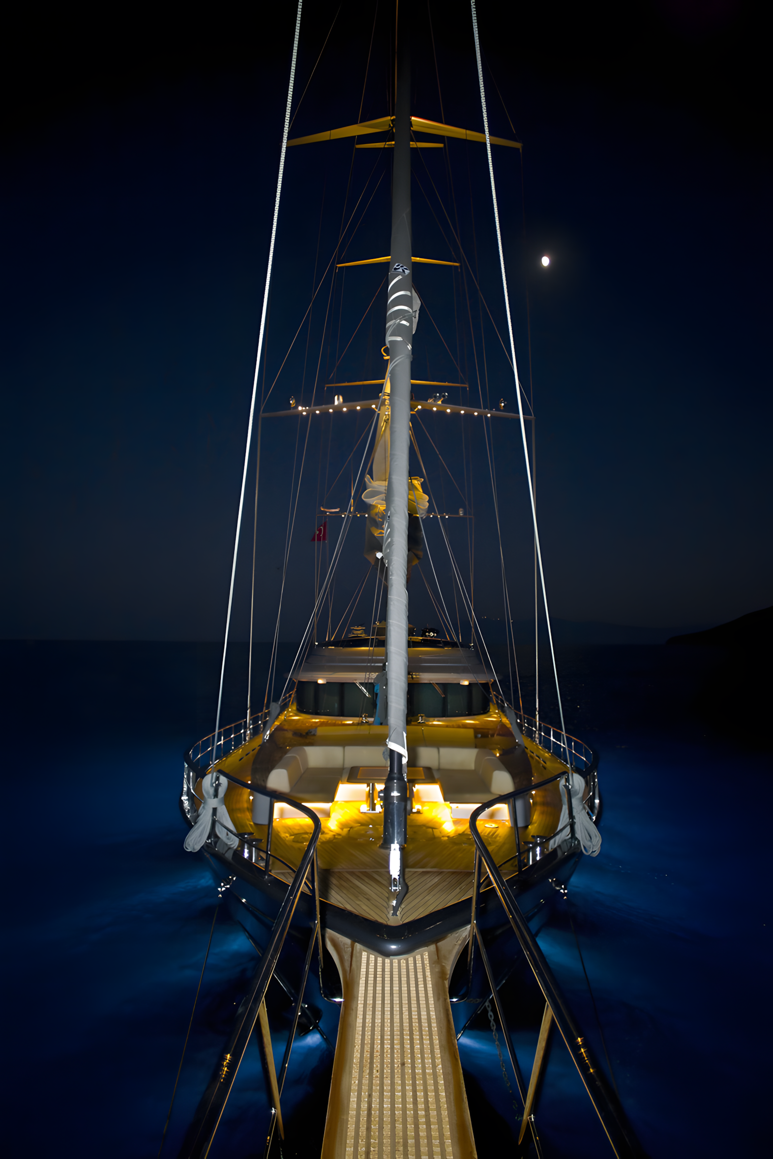 View of a luxury yacht at night, illuminated by onboard lights, with a moon in the dark sky.