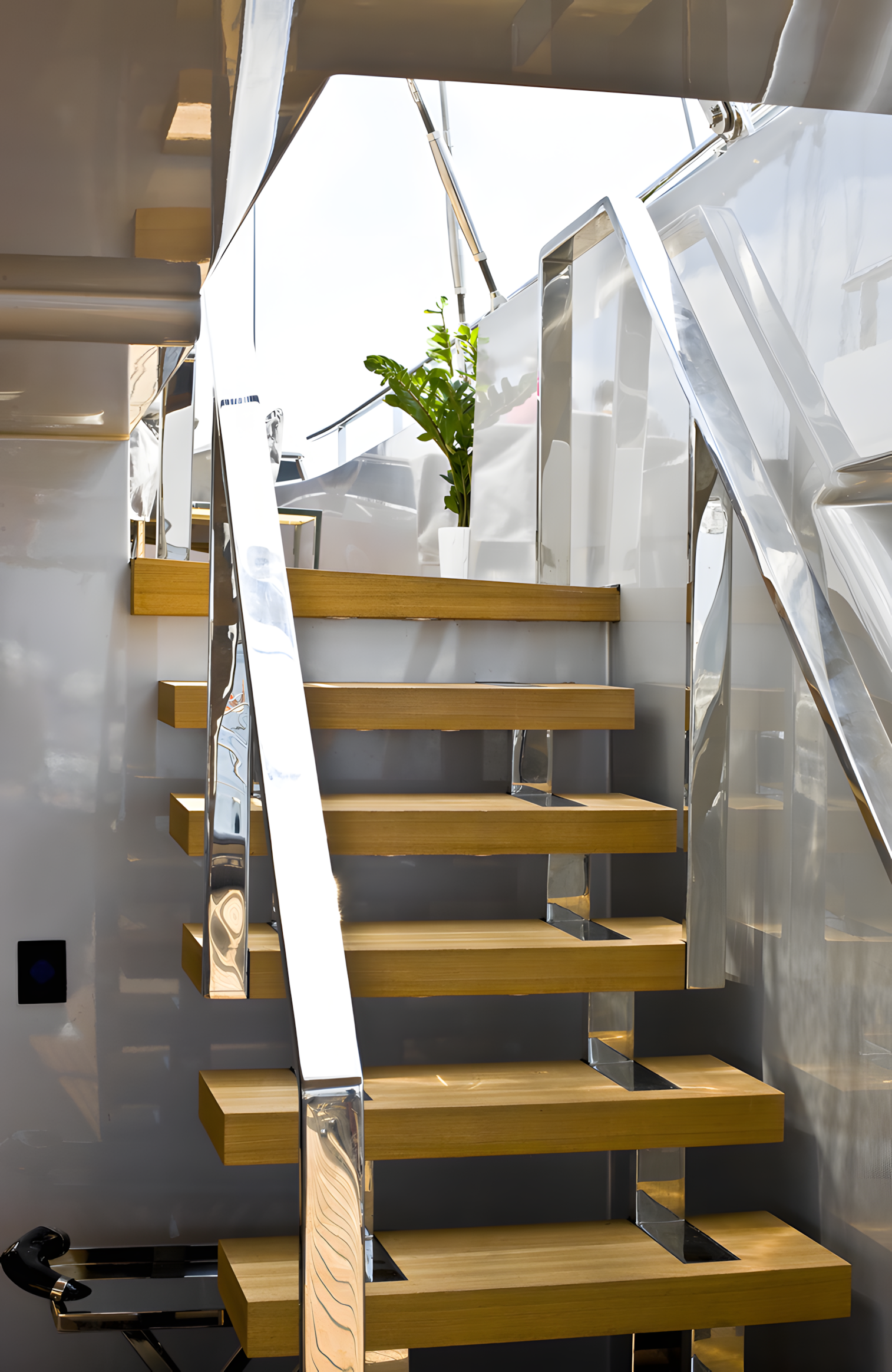 Modern staircase with wooden steps and shiny metal railing leading to an upper deck with a houseplant near the top.