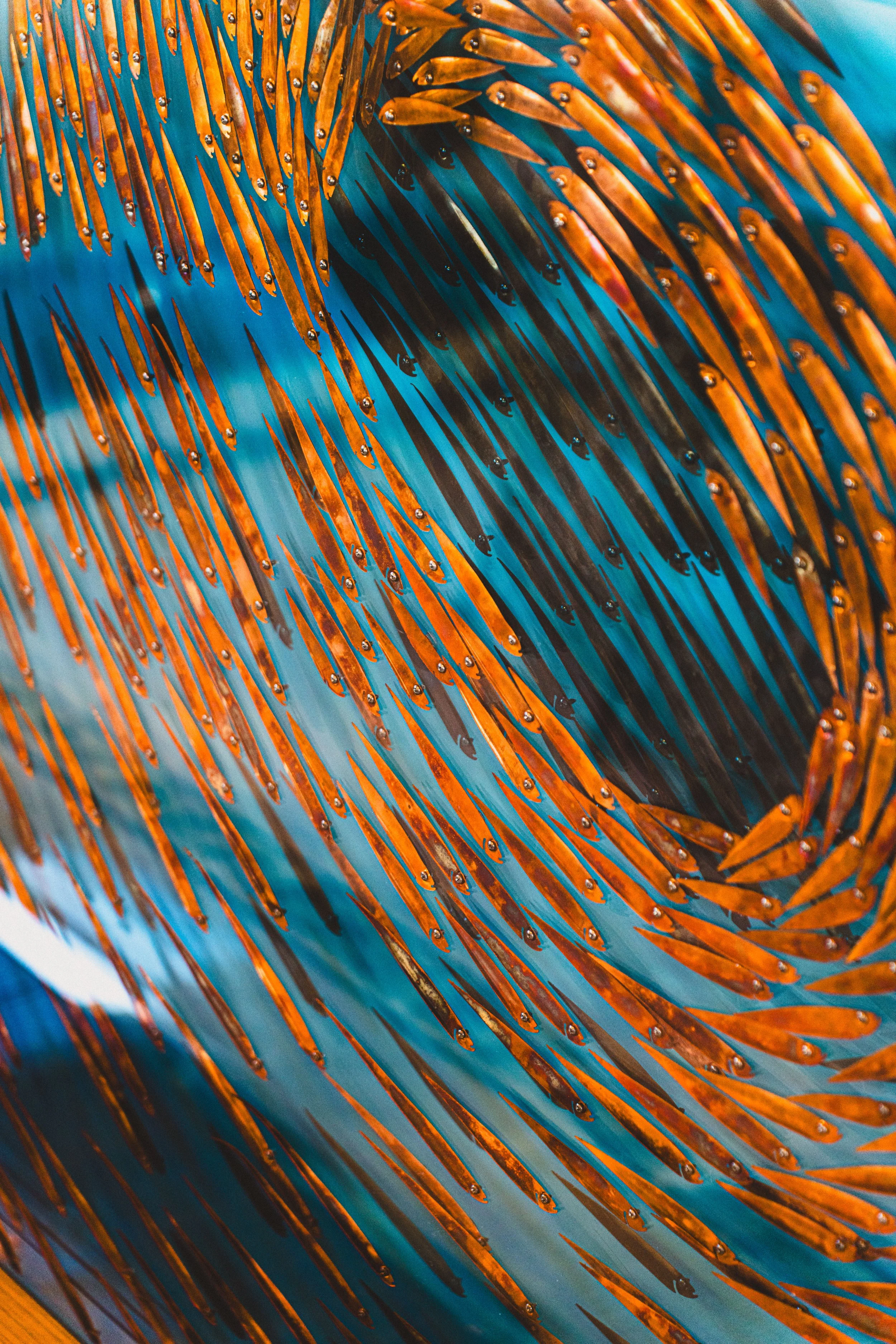 Close-up of a metallic, orange and black spiral sculpture with a blue background.