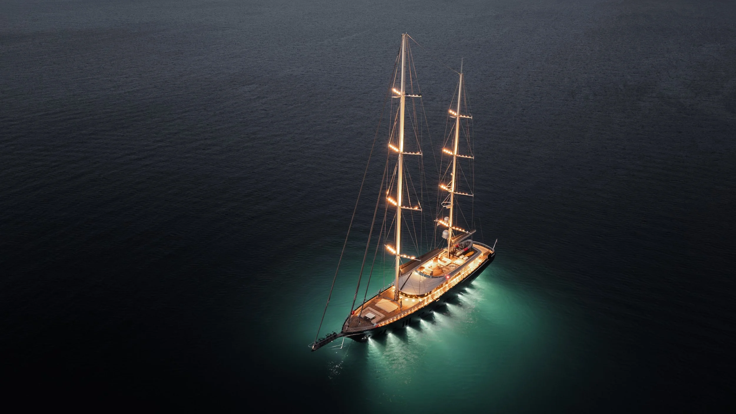 An illuminated sailboat with two masts on dark water at night