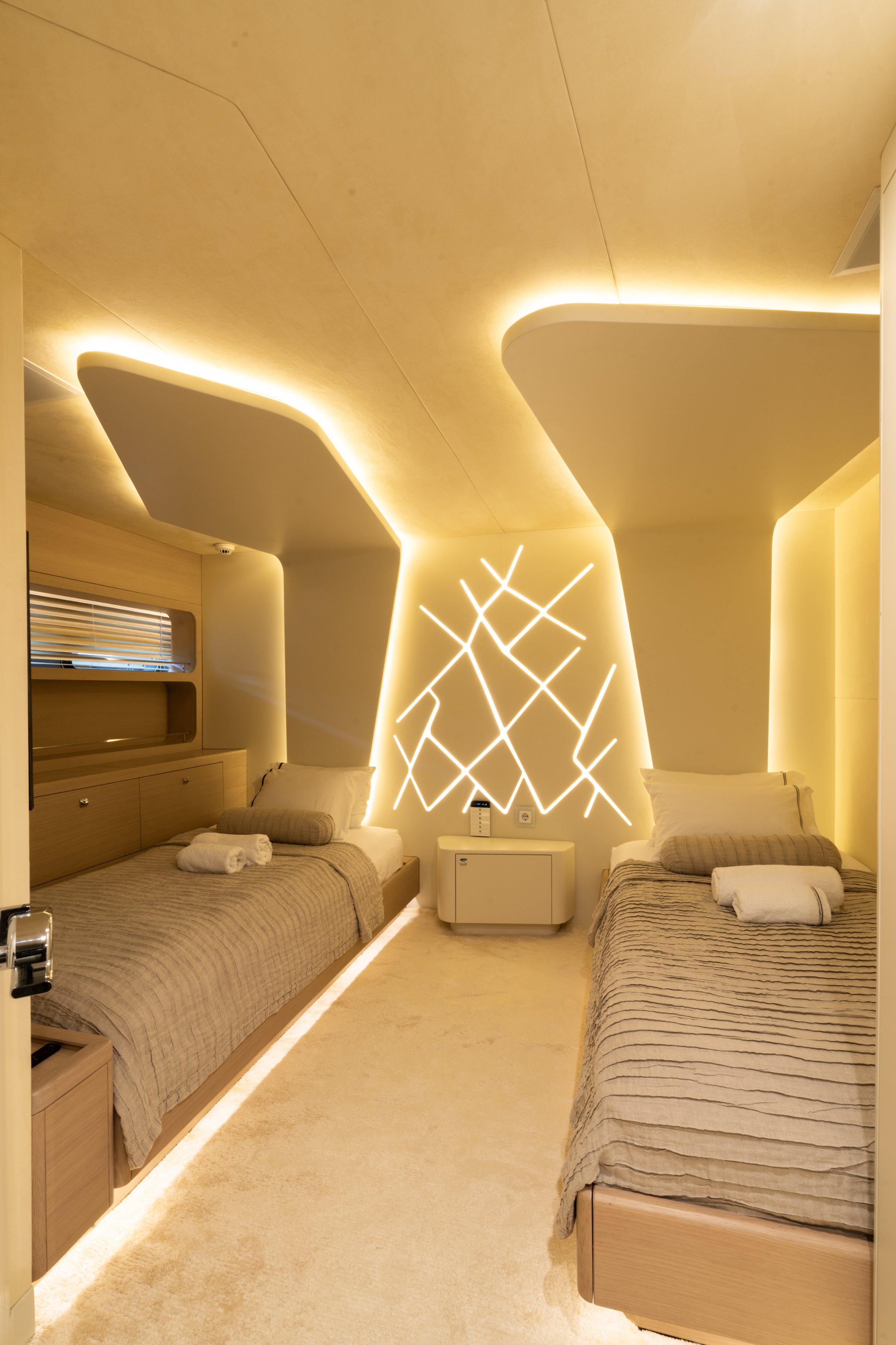 A modern hotel room with two beds, each with neatly folded towels on top, and illuminated curving ceiling designs with neon lighting on the wall.