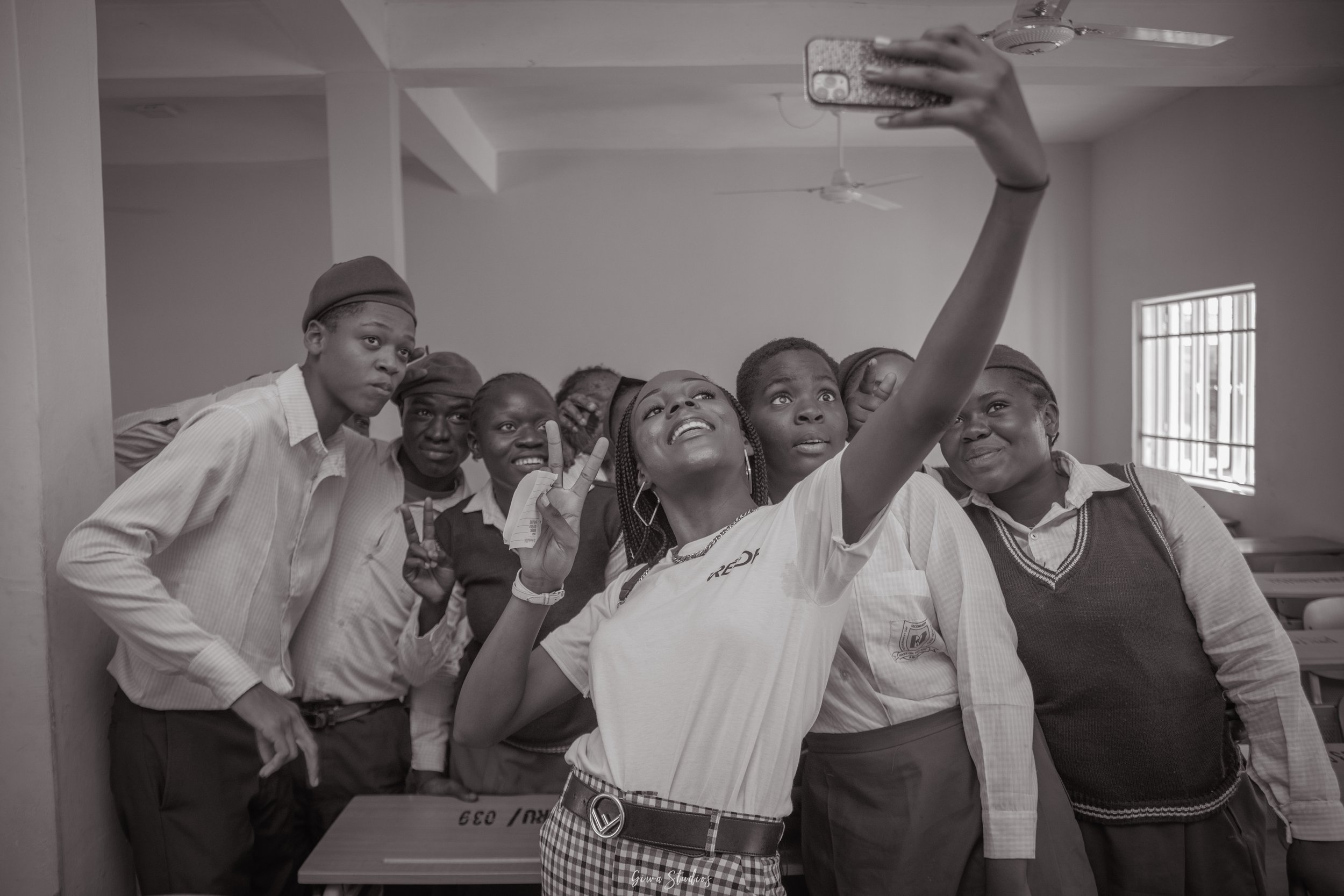 A group of students taking a selfie in a classroom, with some students making peace signs and smiling.