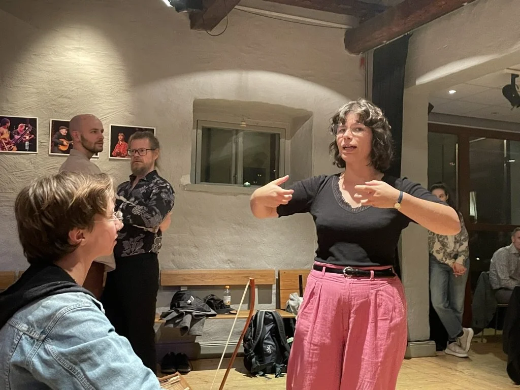 Leonora förklarar något om fattningen med armarna framför sig, som. om att hon skulle krama någon.