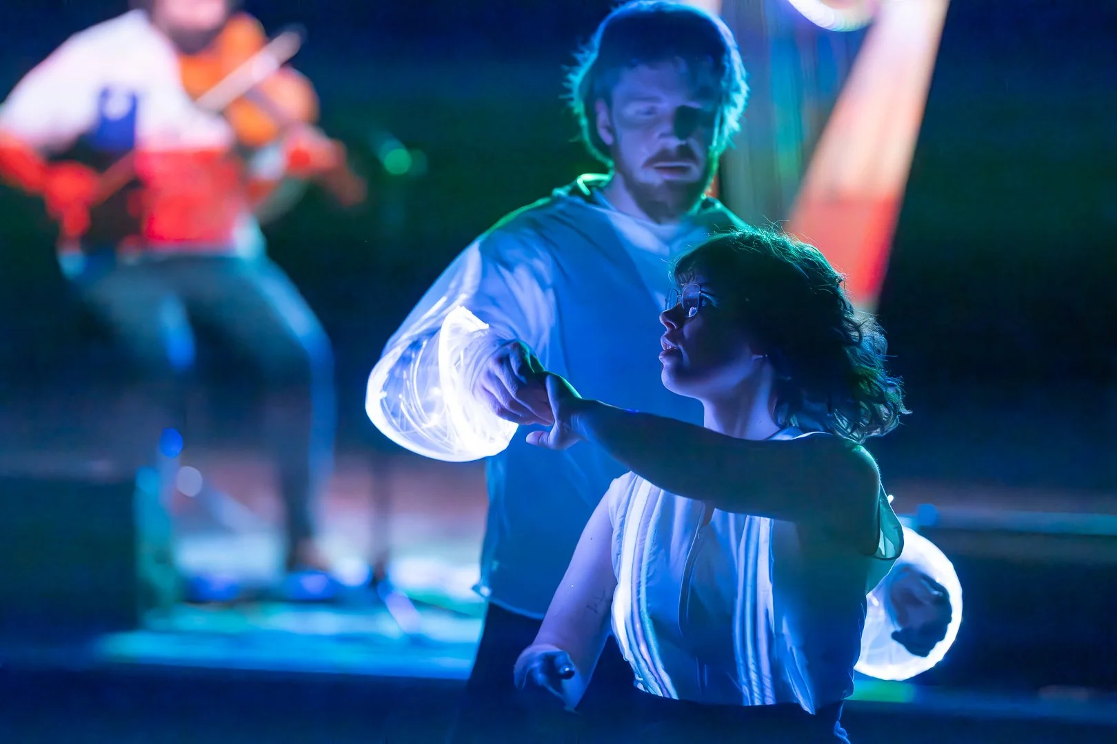 The dancers Leonora and Martin are holding hands in a turn. The picture is from the show "Blåt Lys en balinstallation", their custumes are uplit by LED lights.