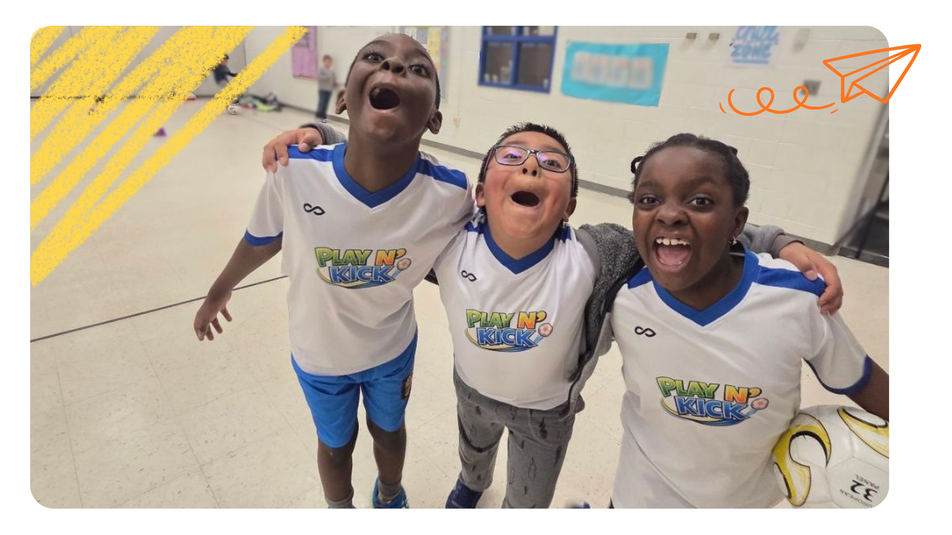 Three children in matching white and blue sports jerseys smiling and cheering indoors, with their arms around each other.