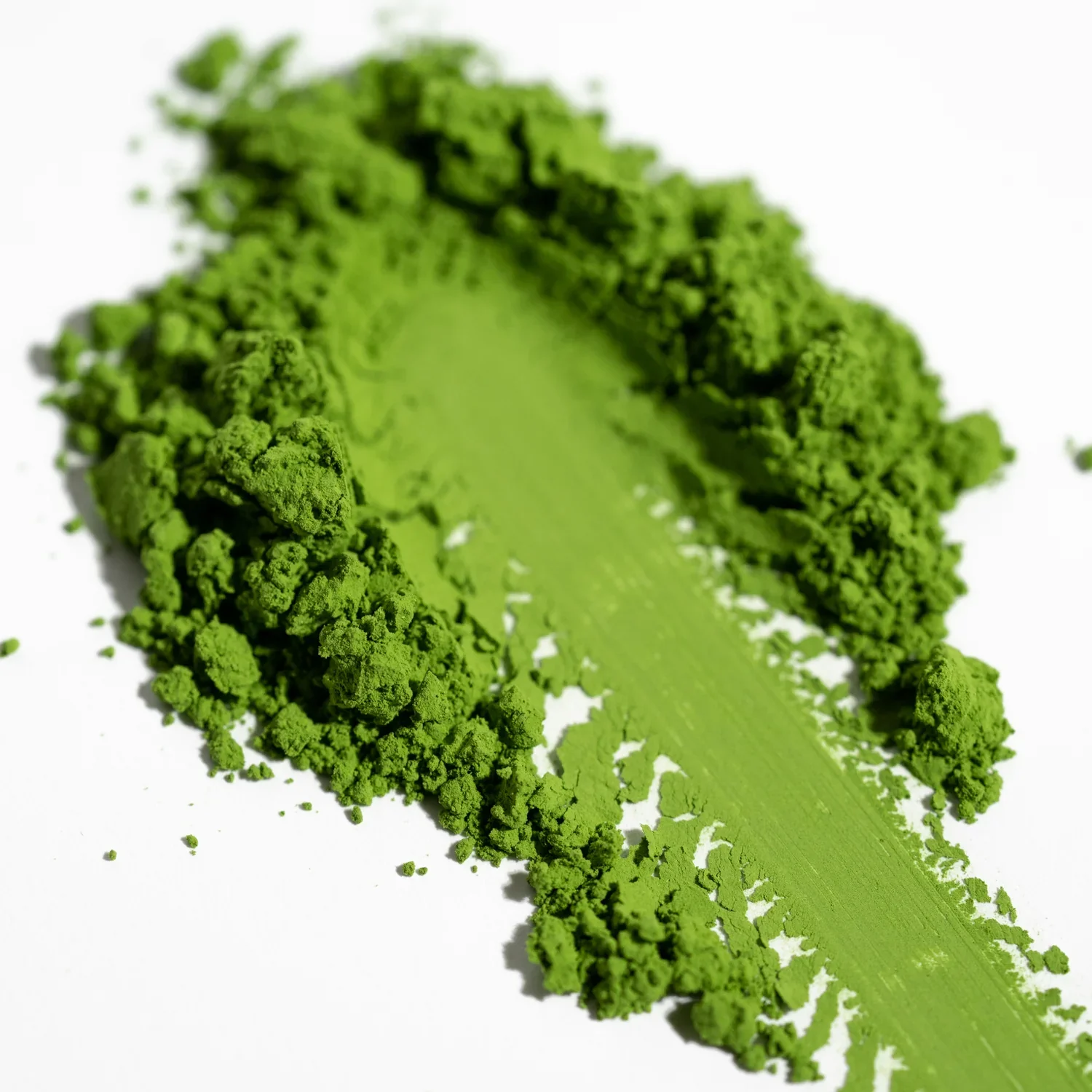 Bright green ceremonial matcha powder smeared across a white background.