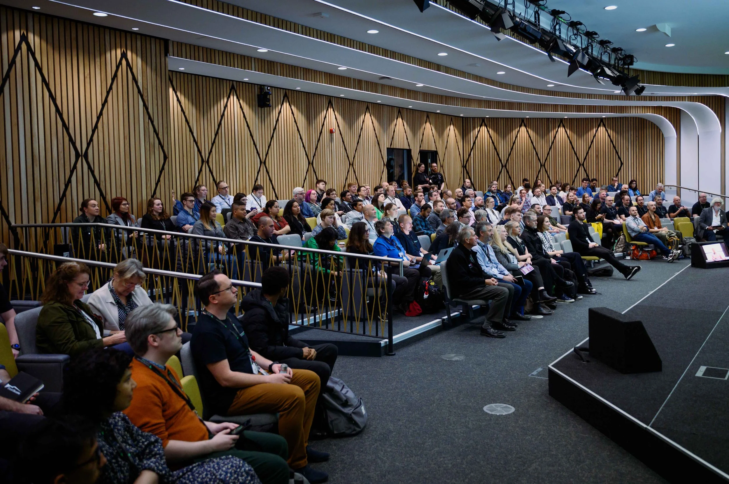 Audience seated in a large auditorium watching a presentation on stage.