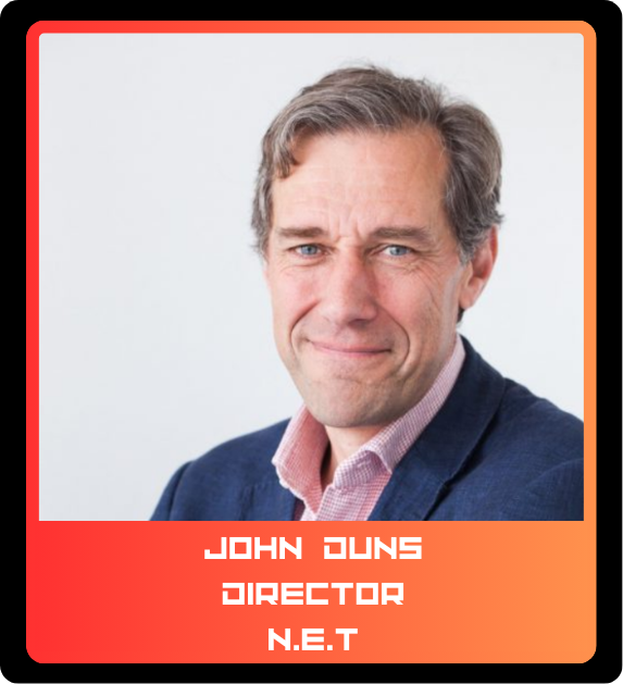 A professional headshot of a man with gray hair and blue eyes, wearing a dark blue blazer and a light pink shirt, smiling slightly against a plain light background.