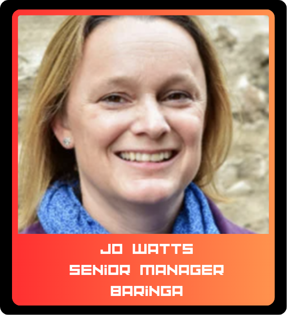 A woman with shoulder-length blonde hair smiling outdoors, wearing a blue scarf and purple top.