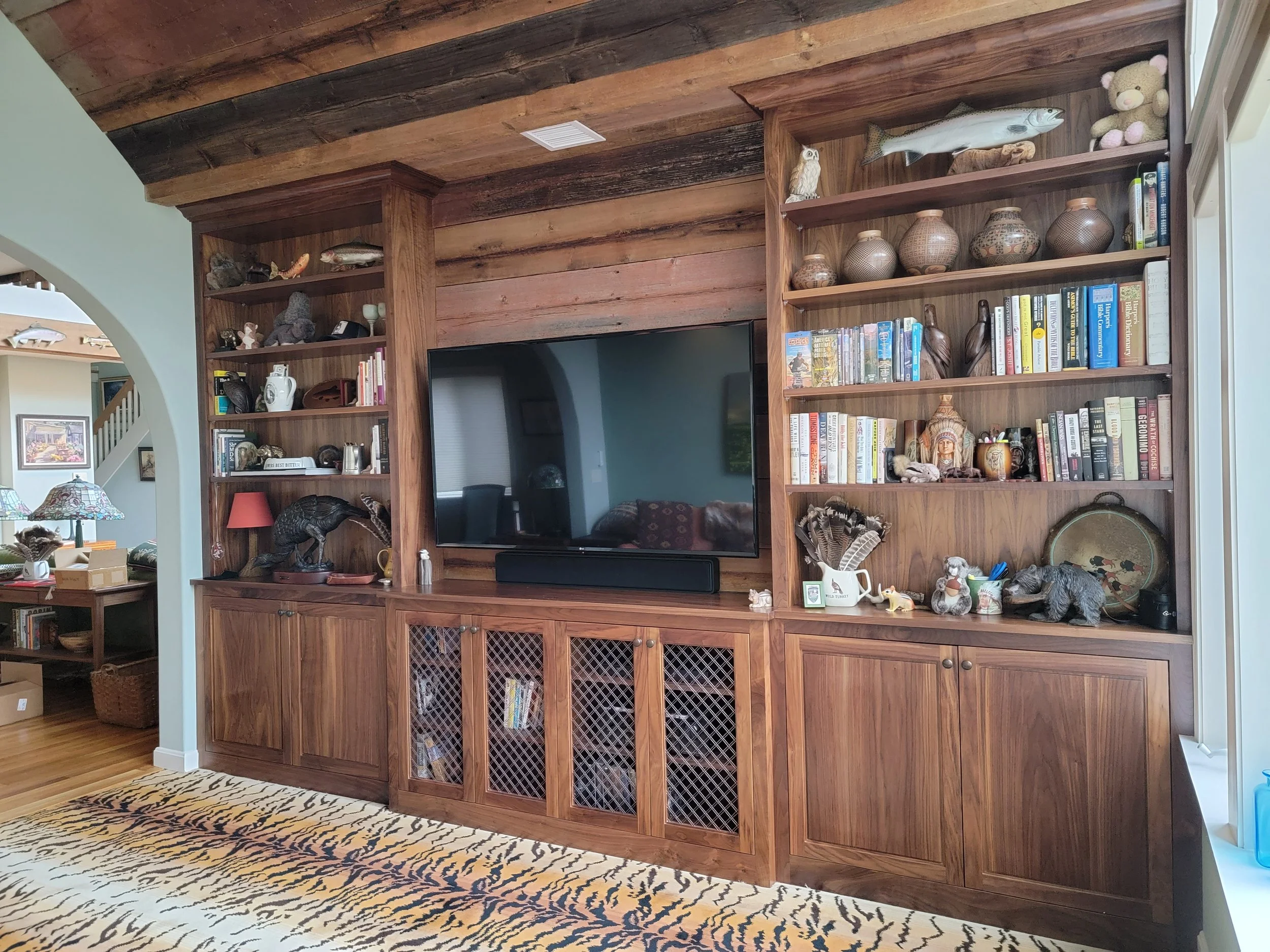 Wooden built-in bookshelf with decorative items, books, and a large flat-screen TV in a living room.