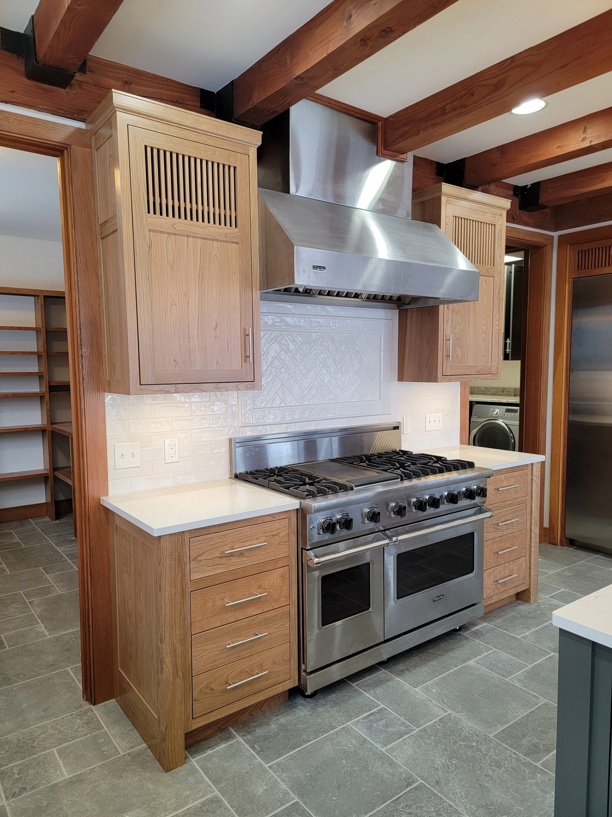 Kitchen with wooden cabinets, stainless steel range and hood, white backsplash, and gray tiled floor.