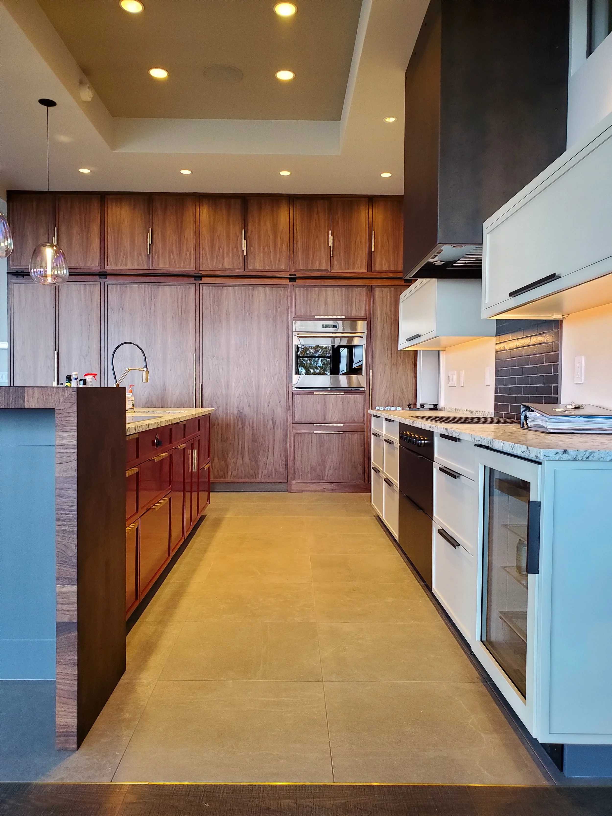 Modern custom kitchen with walnut cabinetry, white perimeter cabinets, large island with waterfall countertop, built-in appliances, and recessed ceiling lighting in a high-end residential home.