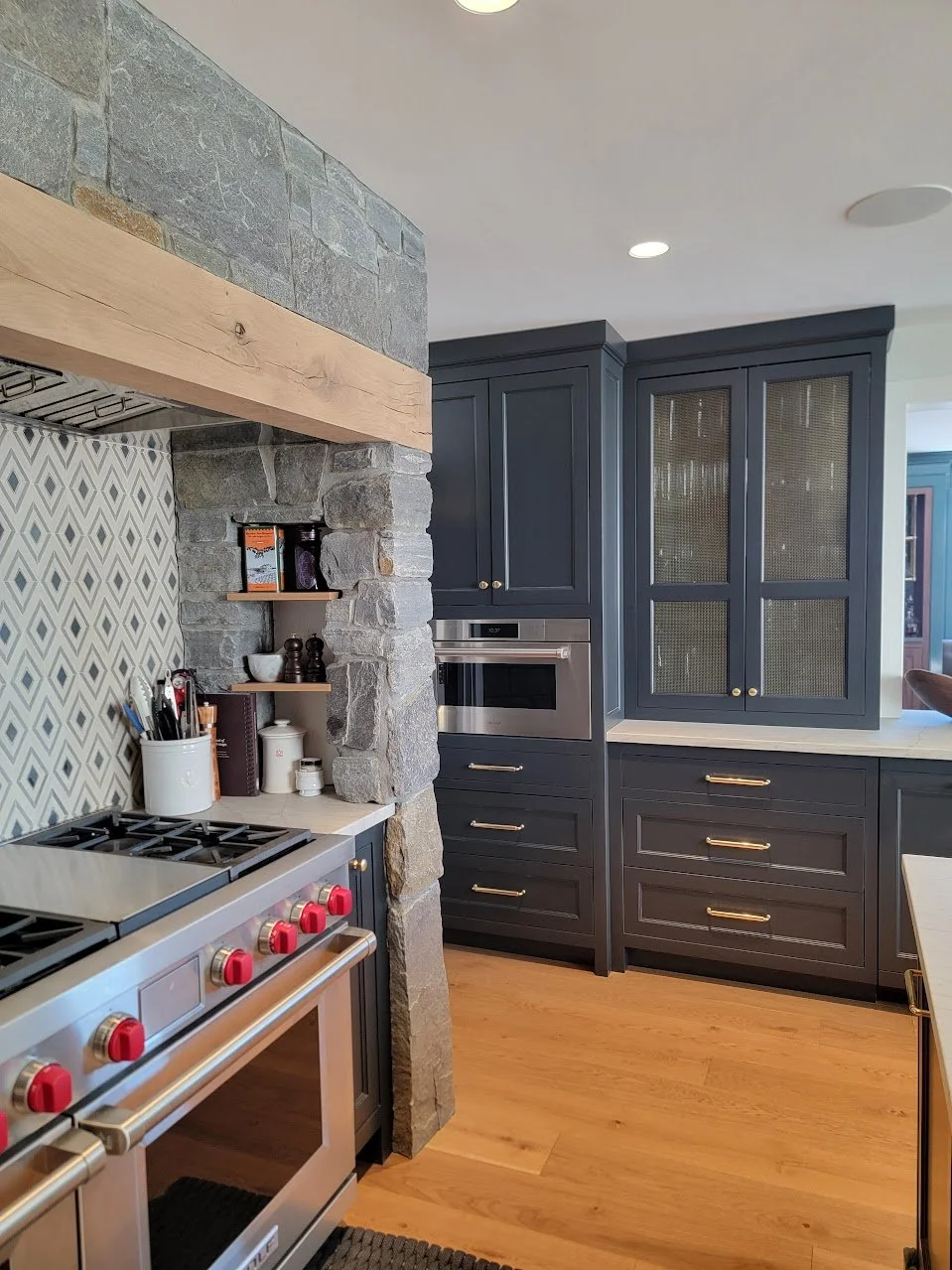 Stone-clad range hood and cooking wall framed by charcoal cabinetry and transitional millwork detailing.