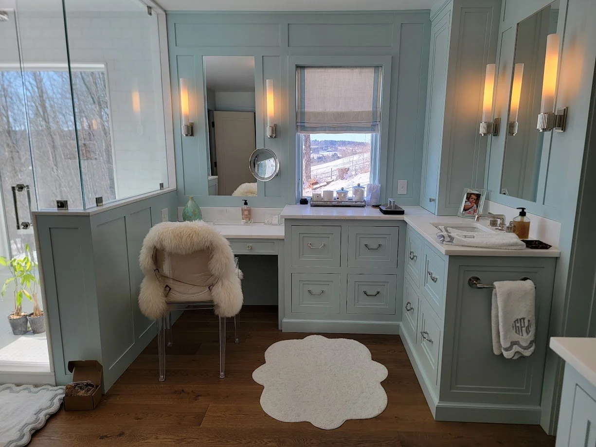 His-and-hers primary bathroom vanity with custom makeup desk in soft blue, featuring built-in storage and tailored millwork details.
