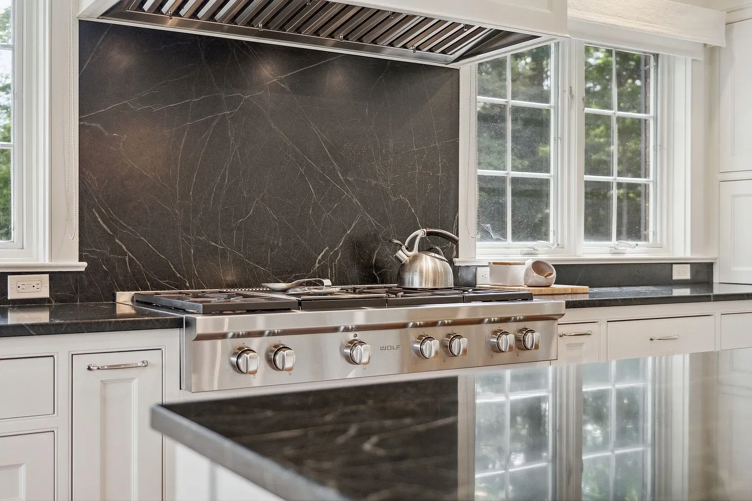 Modern kitchen with black marble backsplash, stainless steel gas stove, white cabinetry, and large windows.