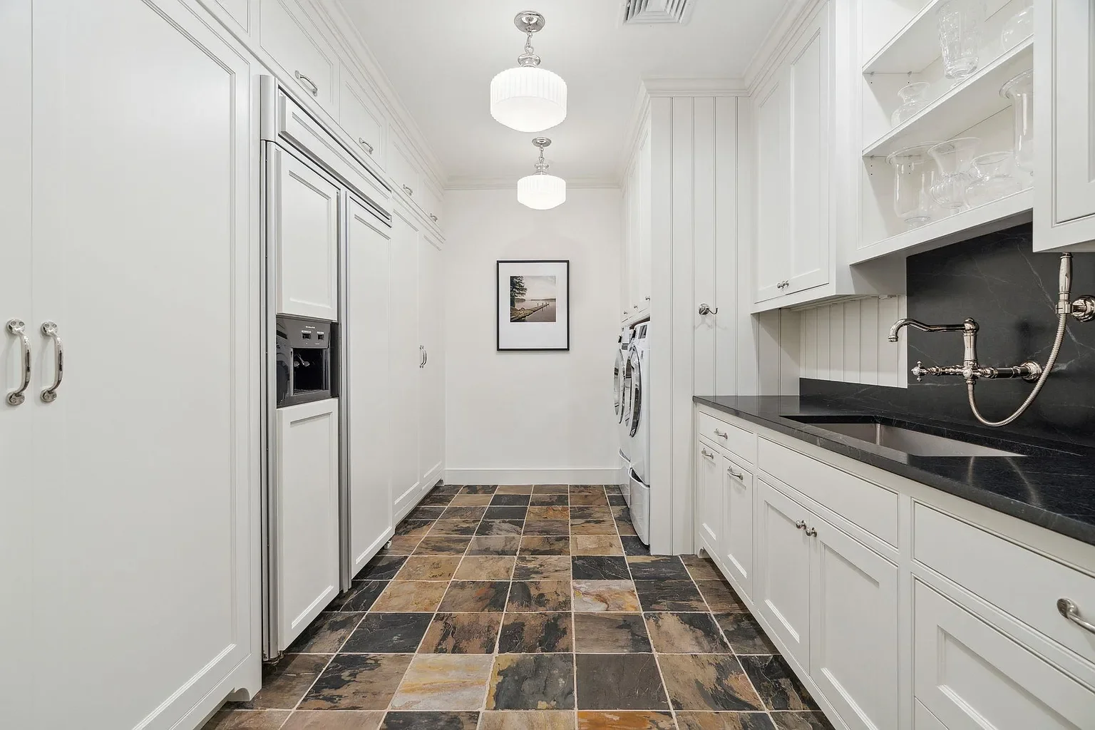 Laundry room with white cabinets, black countertop, washer and dryer, black tile backsplash, and slate tile floor, ceiling lights, and framed picture on the wall.