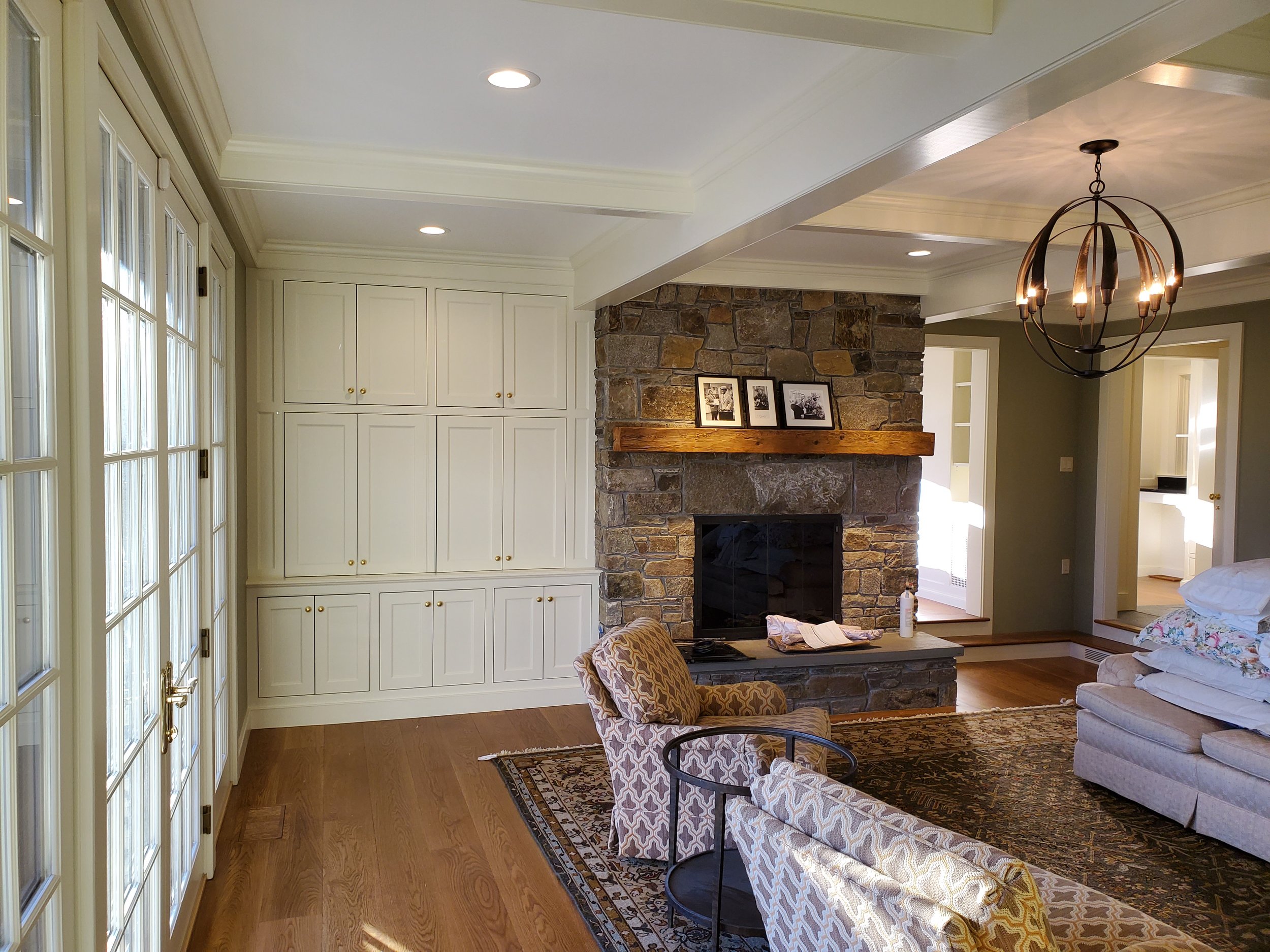 Living room with a fireplace, white built-in cabinets, a chandelier, and armchairs, with French doors on the left side