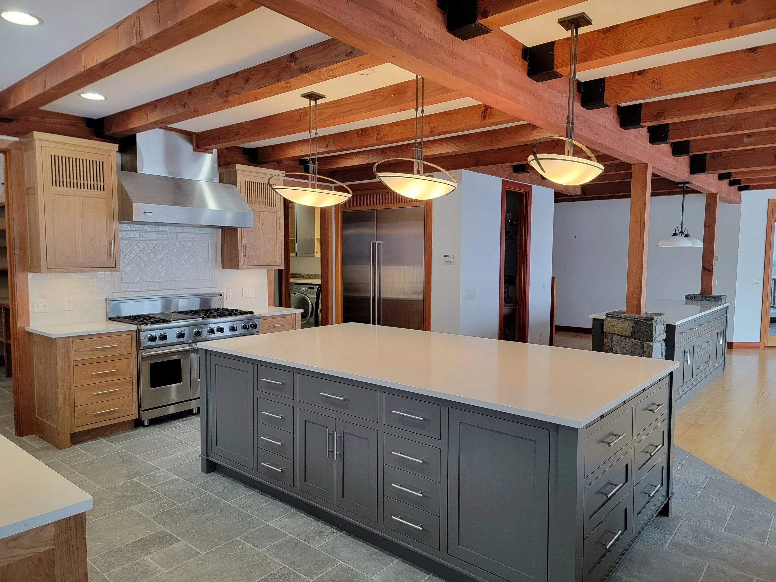 Modern kitchen with gray island, stainless steel appliances, wooden beams, and white countertops.