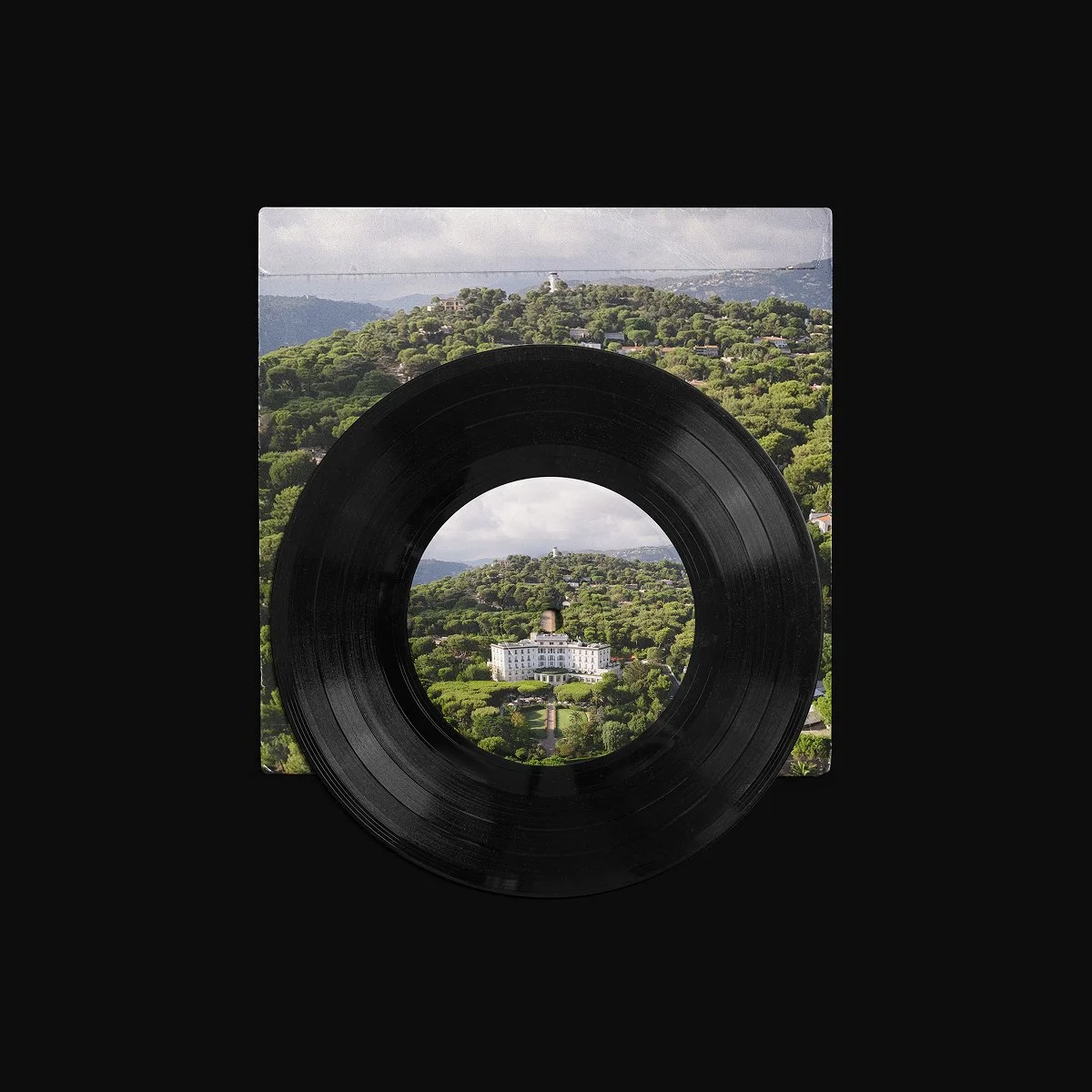 Vinyl record placed on top of a landscape photograph of a lush green hillside with a white mansion at the bottom center, creating a framed view of the landscape through the record's hole.