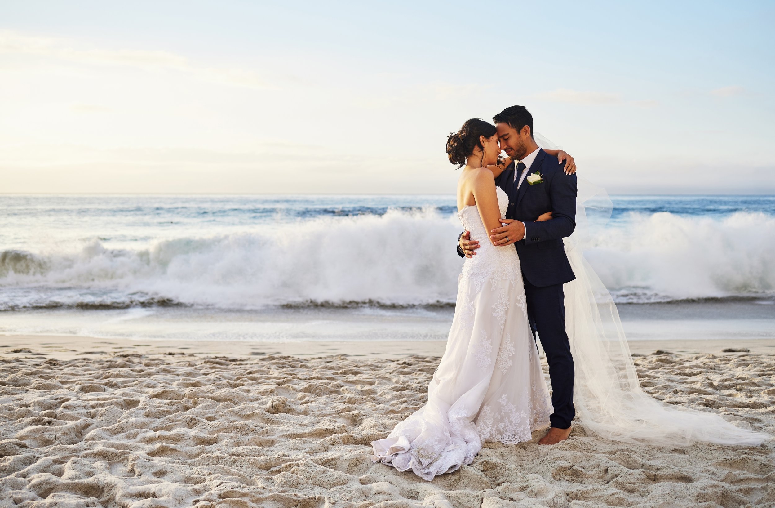A bride and groom hugging and touching foreheads on the beach during their wedding, with waves and the ocean in the background. Chris Zilm marriage celebrant officiating an outdoor wedding ceremony in Brisbane North Queensland