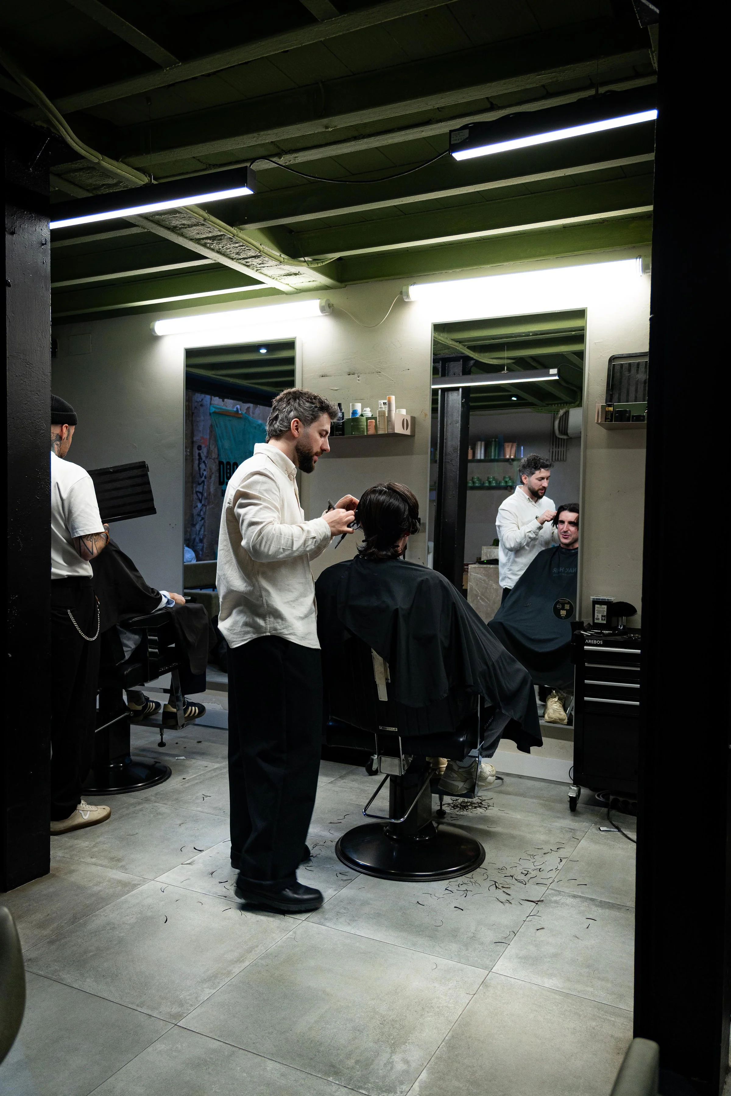 Barbershop with two barbers cutting customers' hair, mirrors on the wall, and a modern industrial design interior.