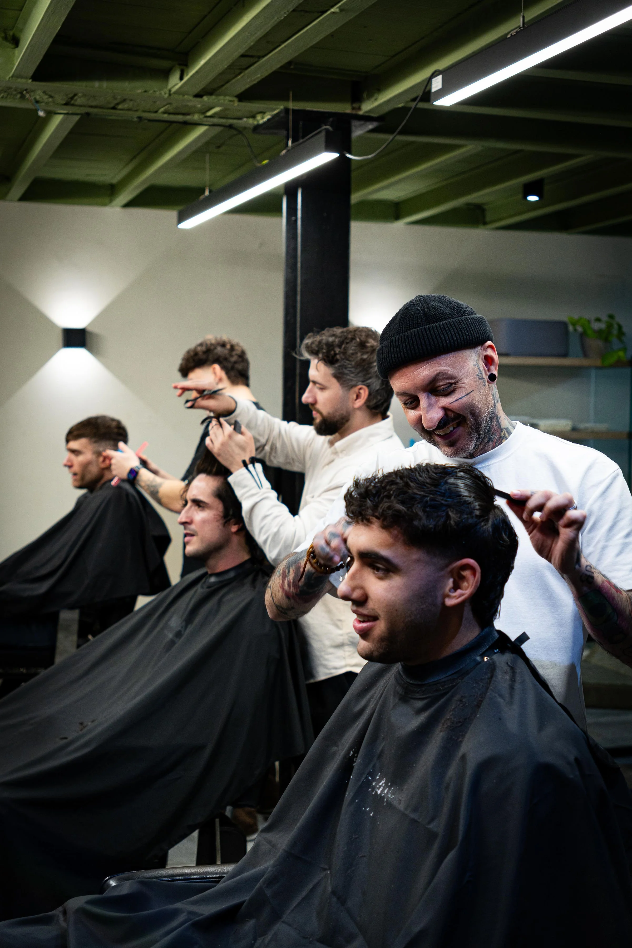 Barbershop scene with three men getting haircuts and stylists working on their hair in a modern, well-lit salon.