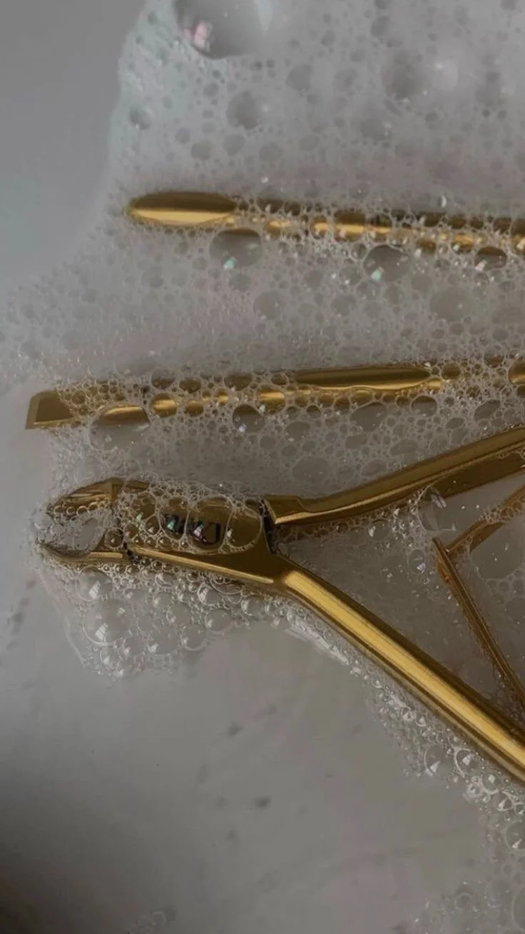 Close-up of metallic gold hair clips partially submerged in soap suds.