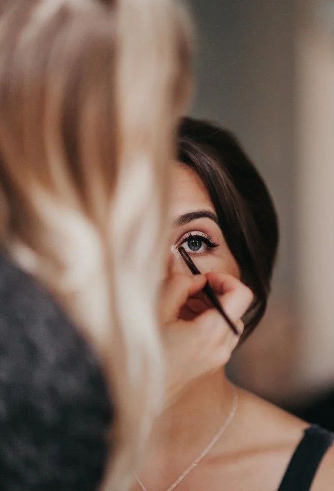 Makeup artist applying eye makeup to a woman with dark hair, focusing on her eye.