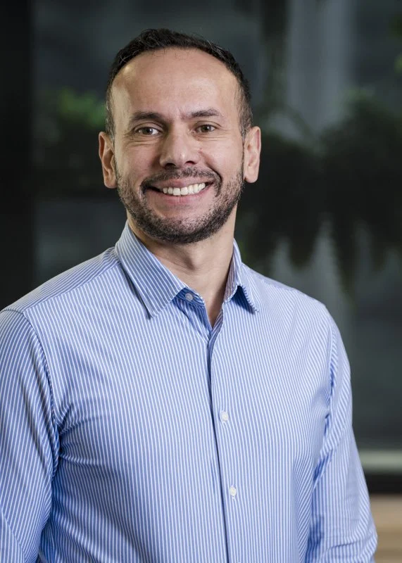 Homem sorridente usando camisa azul em ambiente interno.