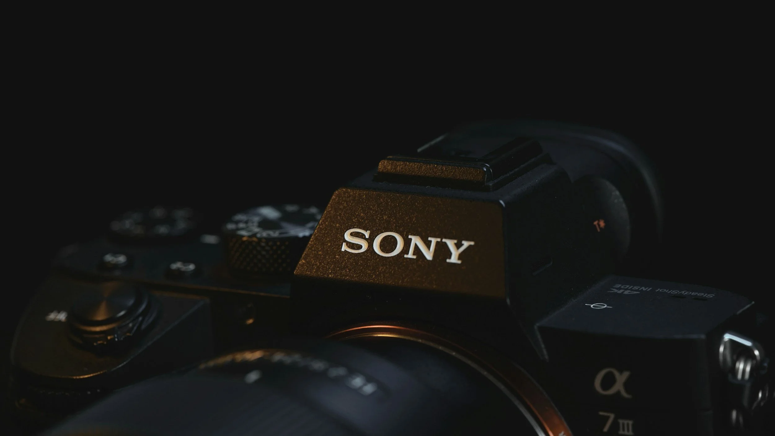 Close-up of a Sony mirrorless camera with a black body, showing the brand logo prominently on the top, set against a dark background.