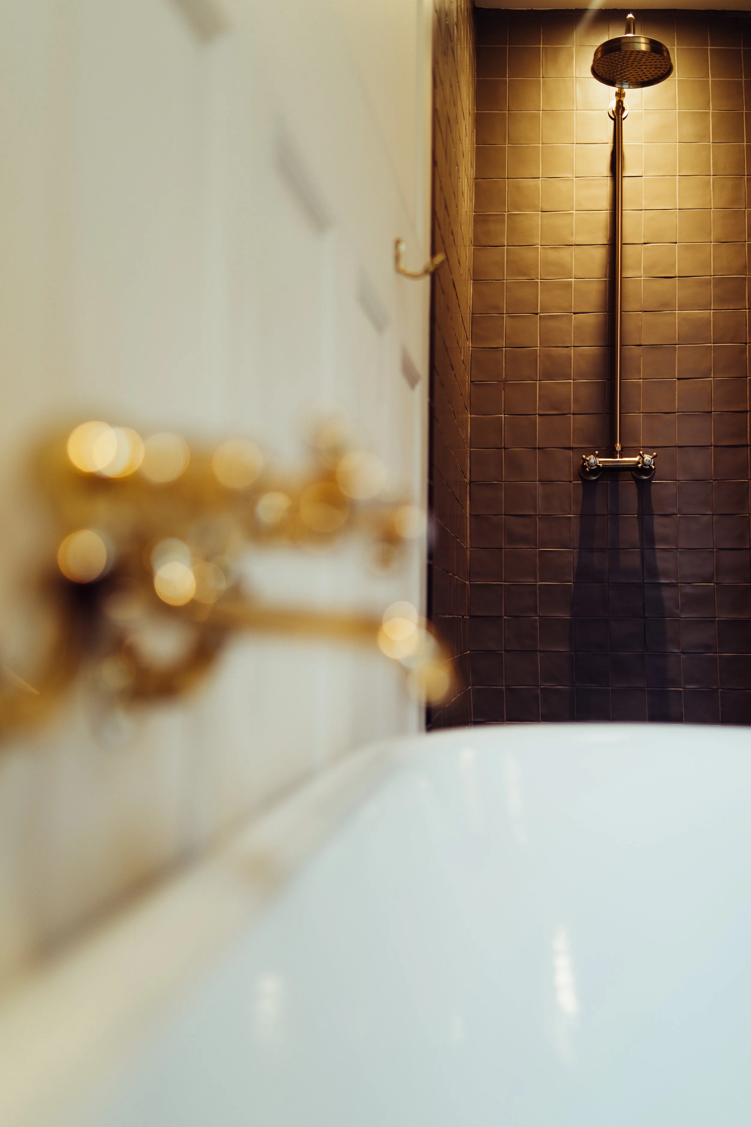 A bathroom with a white bathtub, brass fixtures, and a tiled shower area with a rainfall showerhead on a dark brown tiled wall.