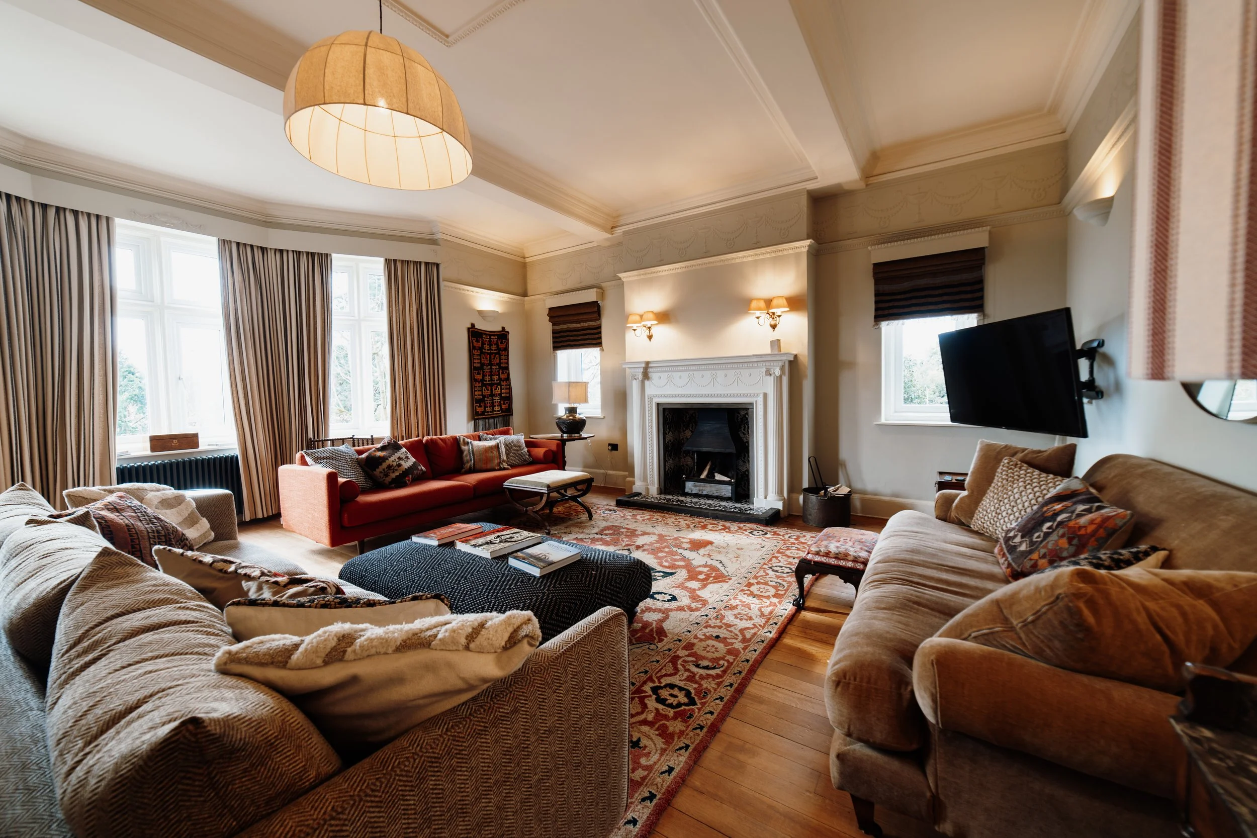 Living room with sofas, armchairs, a fireplace, framed art, a mounted TV, and large windows with curtains.