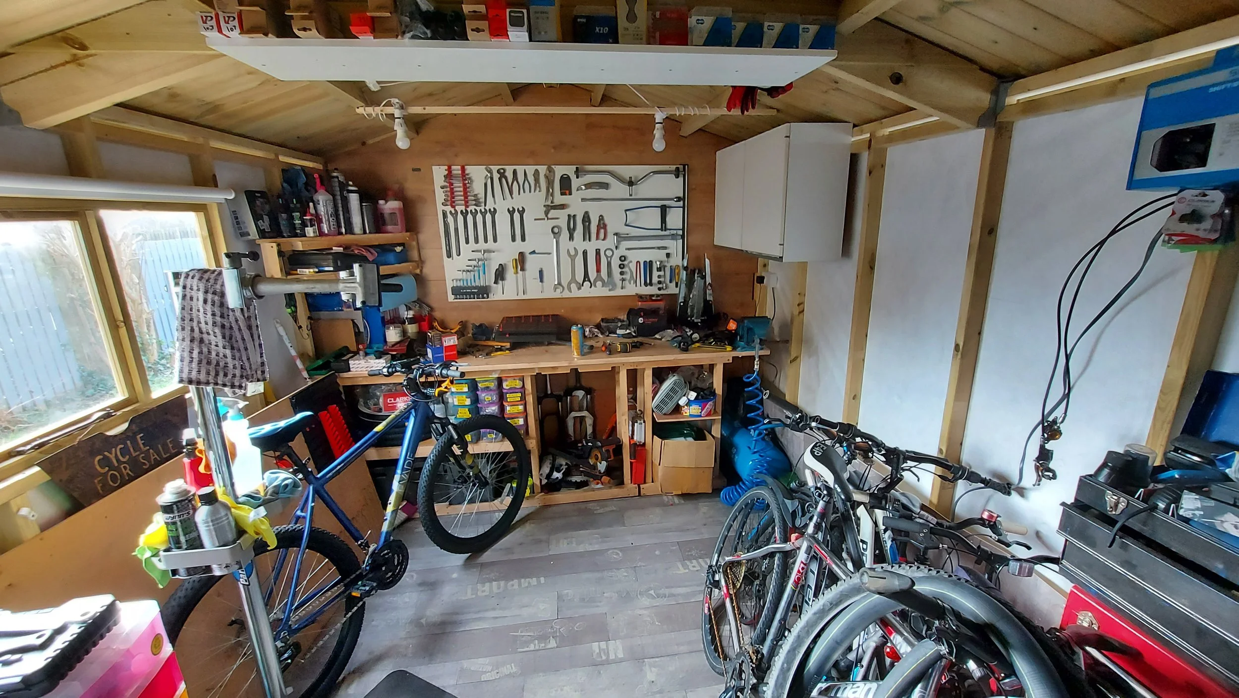 A well-organized garage workshop with bicycles, tools on a wall pegboard, shelves with supplies, and a workbench.
