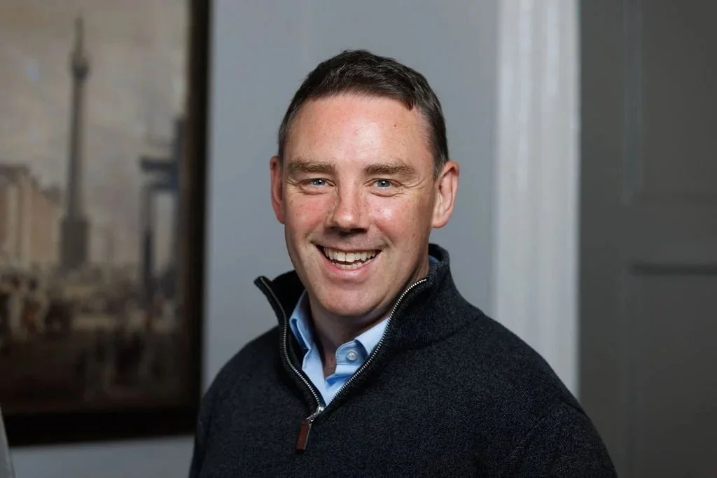 Patrick O'Rourke, a certified career coach, standing indoors with a blurred background and a painting on the wall.