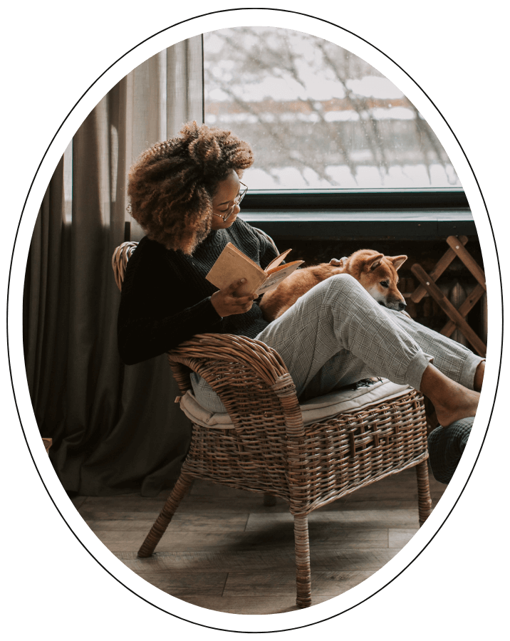 a young woman reading with her dog in a wicker chair.