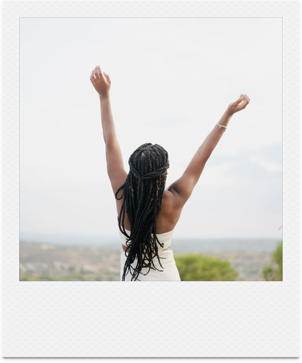 Joyful Black woman in long braid stretching her arms up towards the sky.
