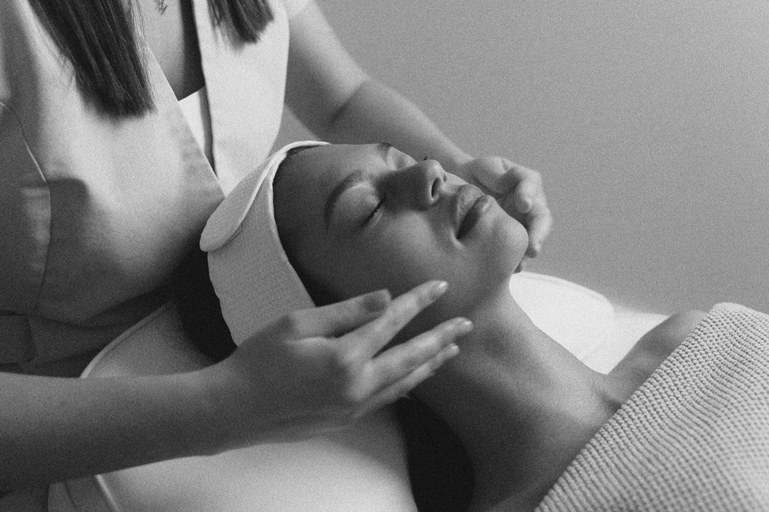 A woman receiving a facial or massage with a towel wrapped around her head, lying down with her eyes closed.