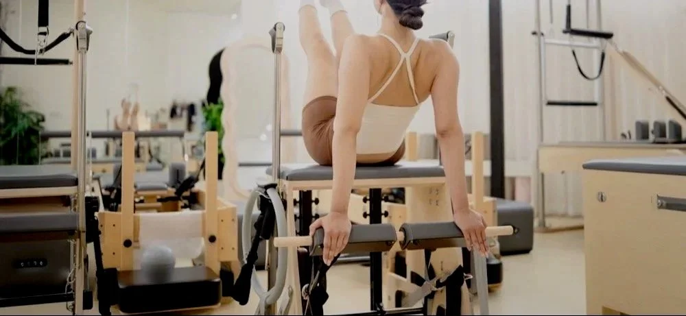 A woman practicing Pilates on a reformer machine in a fitness studio.