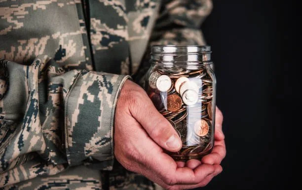 Person wearing camouflage clothing holding a jar filled with coins.