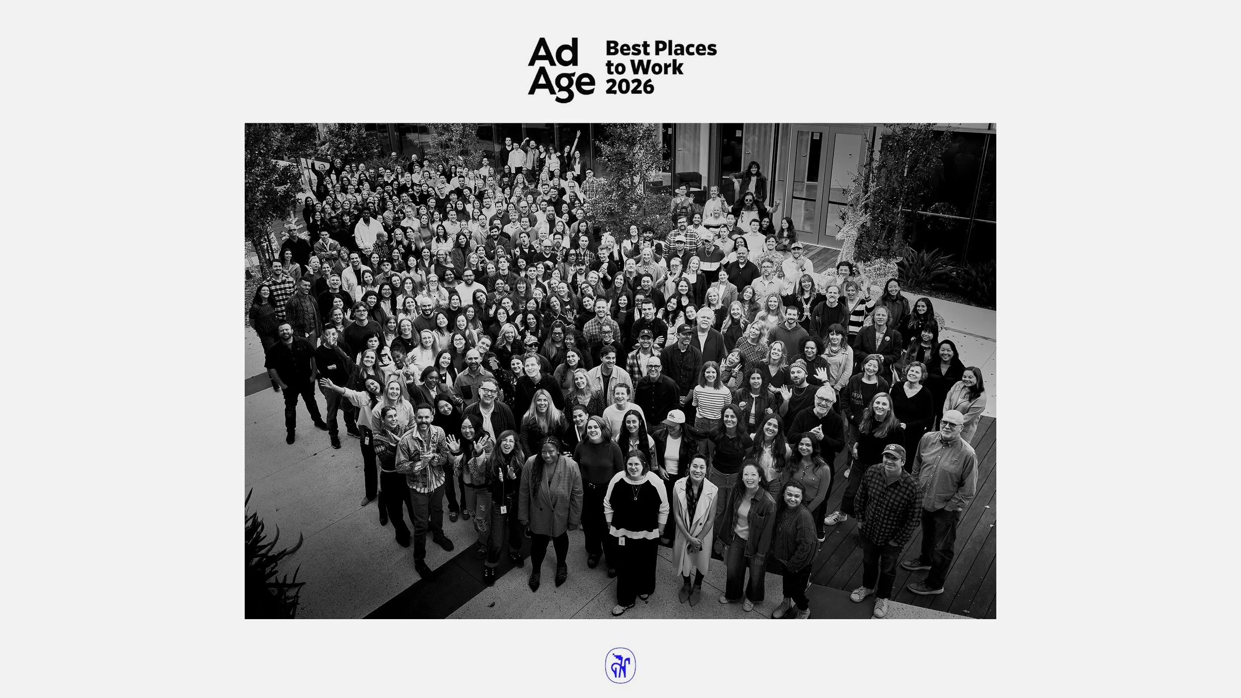 Group photo of people at a corporate event or conference outdoors, smiling and waving, with a diversity of genders and ethnicities, in black and white.