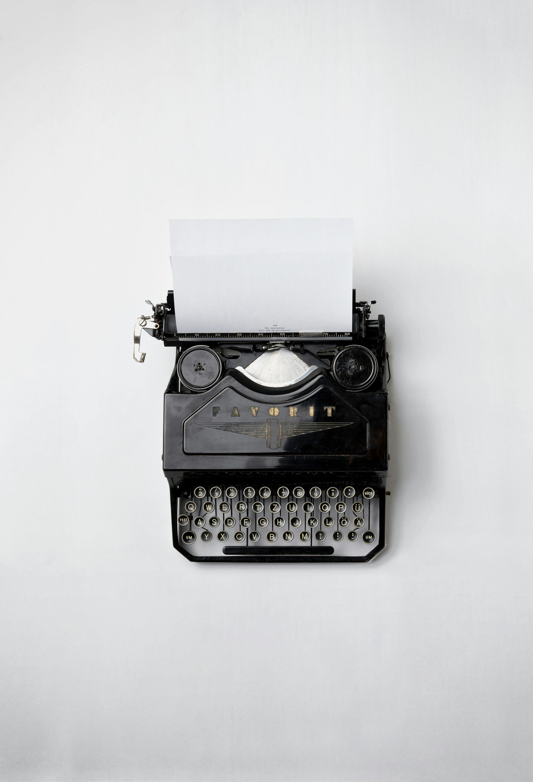 Black vintage typewriter with a sheet of paper, placed on a white surface.