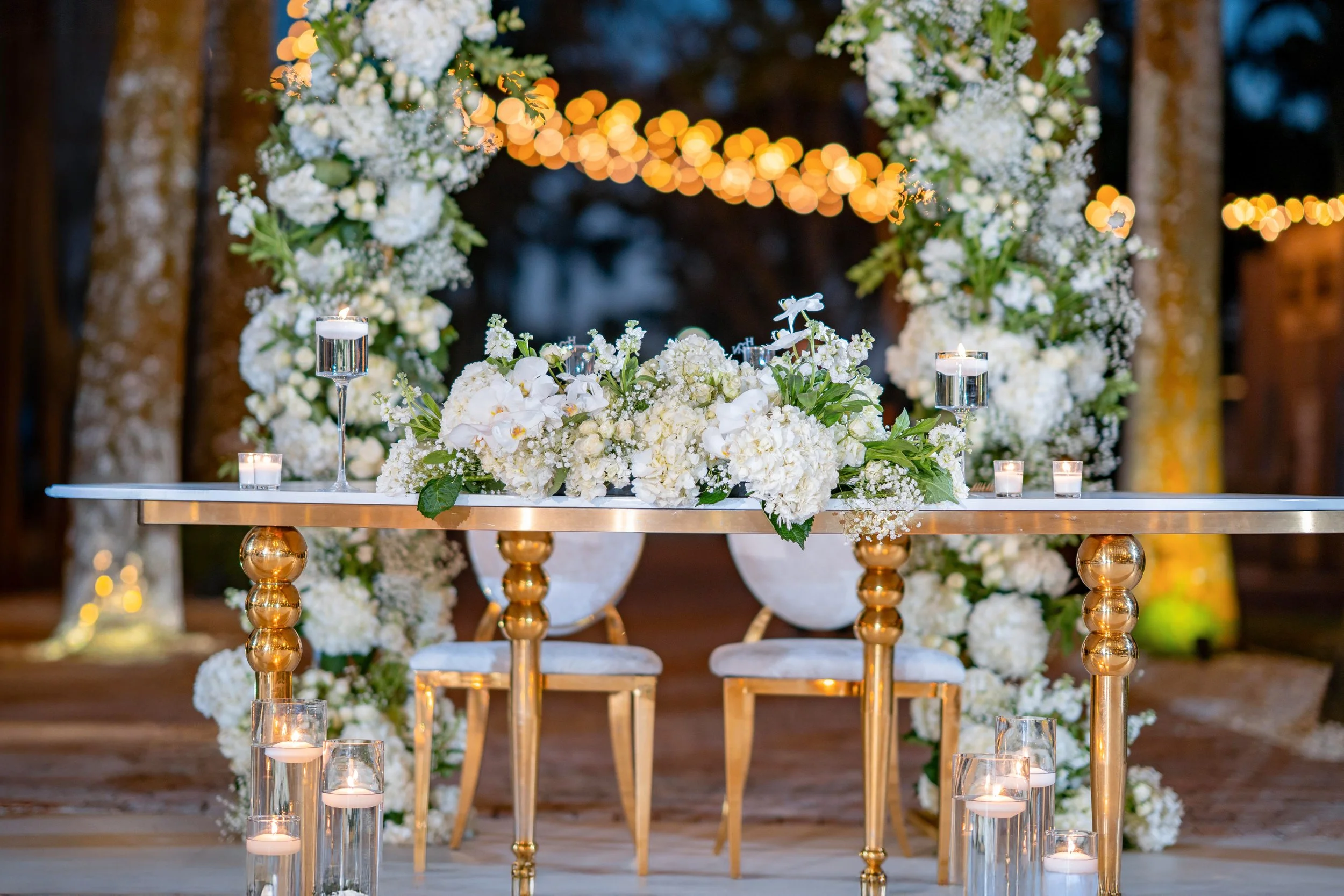 An elegant wedding altar decorated with white flowers, candles, and fairy lights in an outdoor nighttime setting.