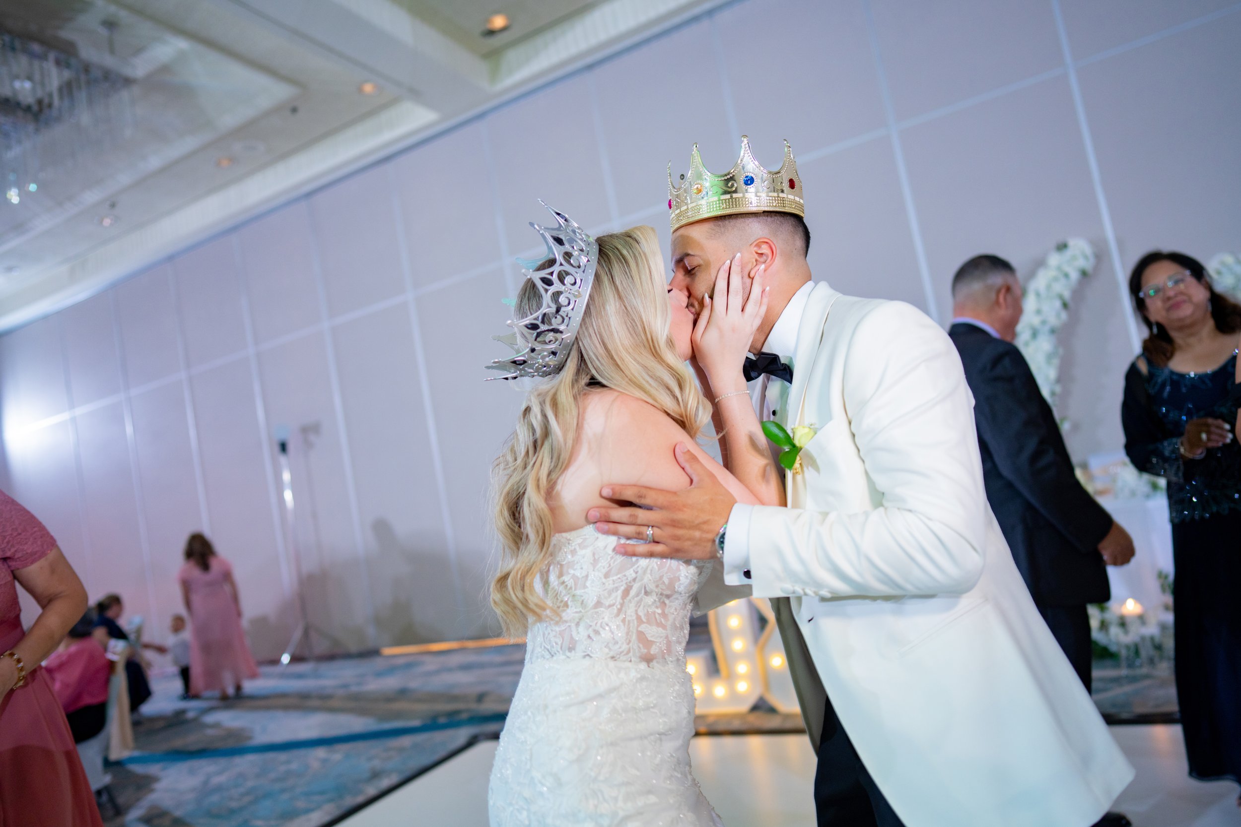 Newlyweds sharing a fun kiss wearing party crowns at HILTON TAMPA DOWNTOWN; energetic wedding reception photography by Star Visual Art, Tampa.